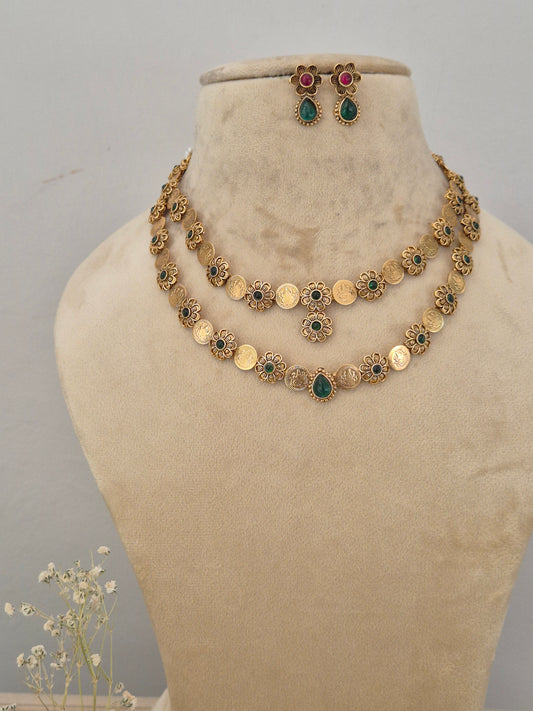 Gold-toned double-layered traditional Indian necklace and matching stud earrings. The necklace features round coin-like disc charms interspaced with green and red floral gemstone accents by naitri.in