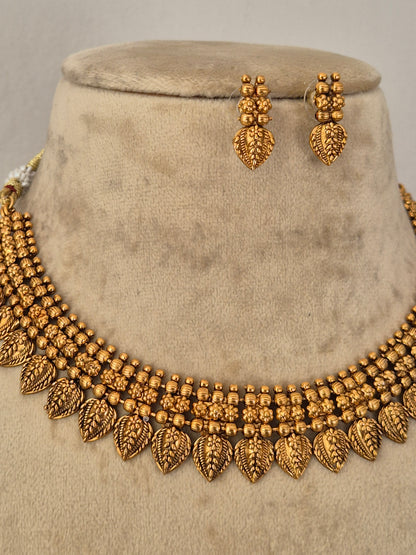Gold-toned traditional jewelry set featuring a beaded necklace with leaf-shaped end pieces and matching drop earrings by naitri.in