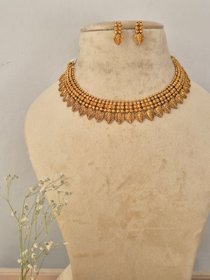 Gold-toned traditional Indian choker necklace and matching dangle earrings set the necklace features intricate, layered textured bead details and a lower fringe of detailed leaf-shaped metallic drops, by naitri.in