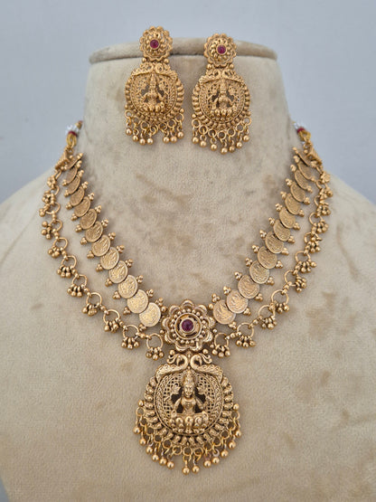 Gold-toned traditional Indian jewelry set featuring a necklace, earrings, the pieces have ornate filigree details, coin motifs, and small red gemstone accents by naitri.in