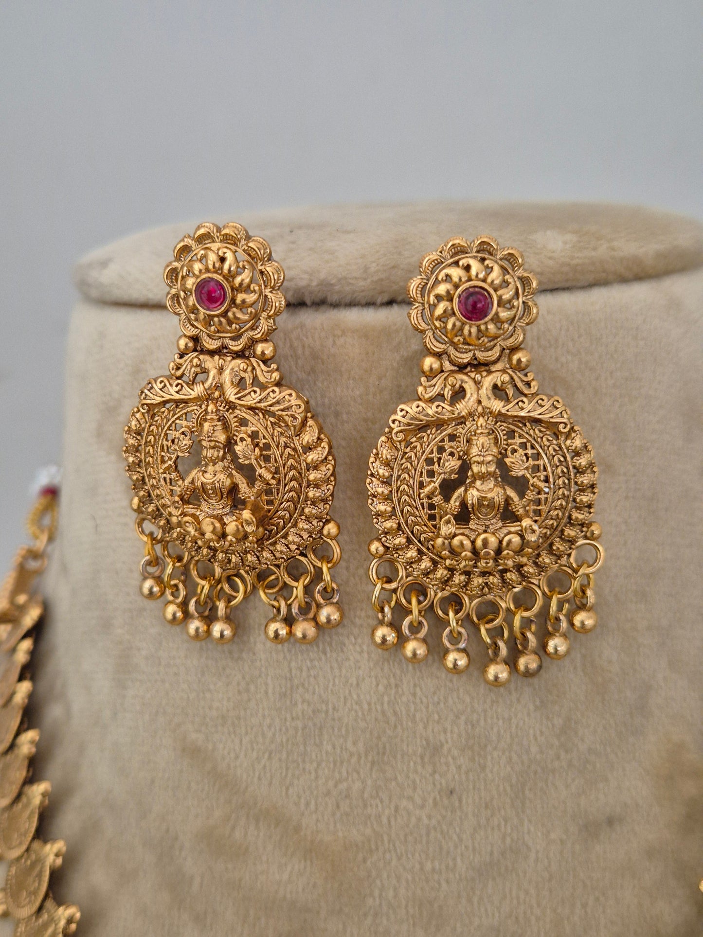 A pair of ornate gold-toned traditional earrings with intricate filigree detailing and small red gemstone accents, by naitri.in
