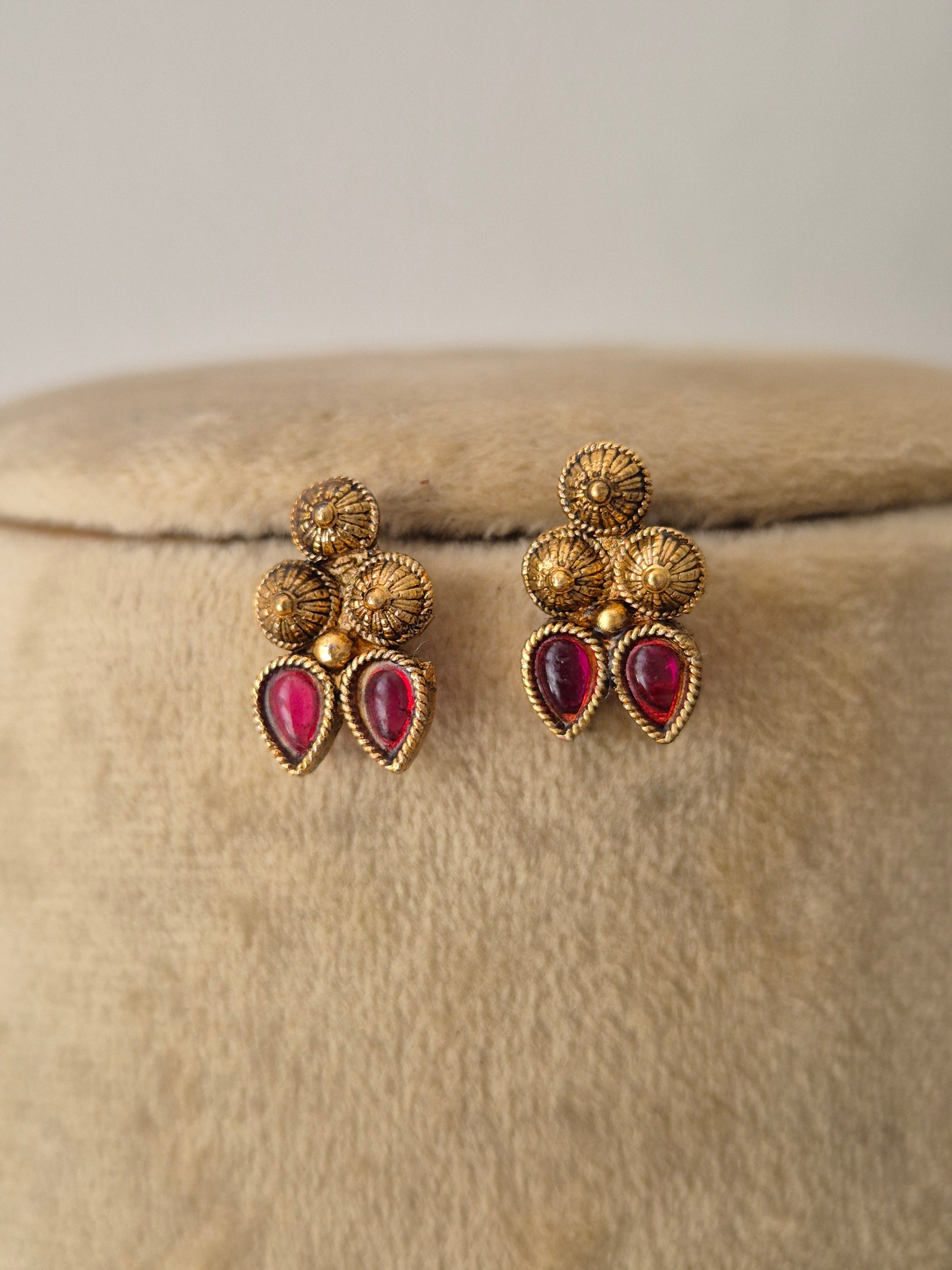 A pair of gold-toned earrings with three round textured beads and two teardrop-shaped pink gemstones, by naitri.in