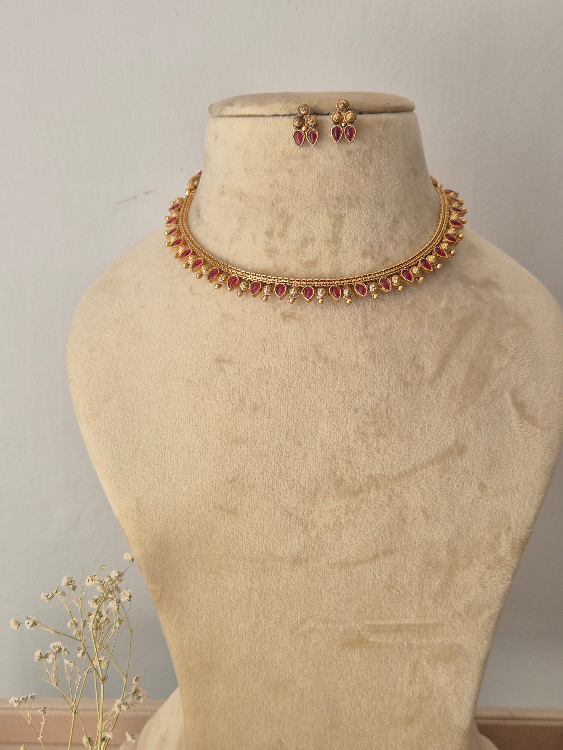 Gold-toned traditional Indian choker necklace and matching stud earrings, choker features a row of vibrant pinkish-red gemstones bordered by textured gold-plated drops, by naitri.in