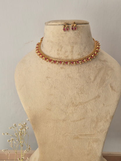 Gold-toned traditional Indian choker necklace and matching stud earrings, choker features a row of vibrant pinkish-red gemstones bordered by textured gold-plated drops, by naitri.in