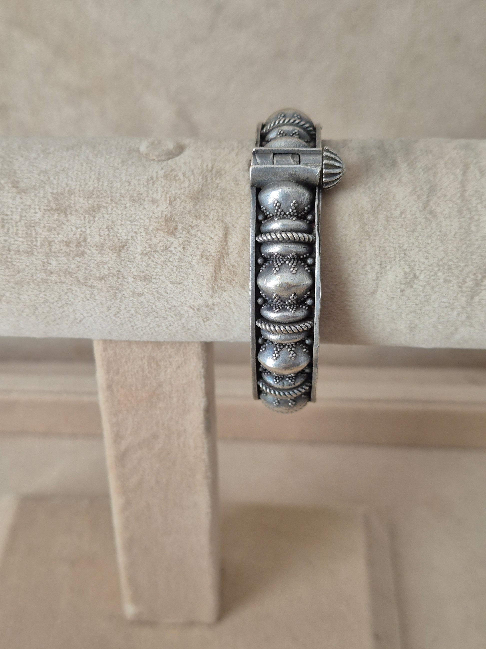 Antique silver oxidized Warisha bangle with textured dome motifs and fine rope-twist borders, displayed on a beige fabric jewelry stand.  by naitri.in
