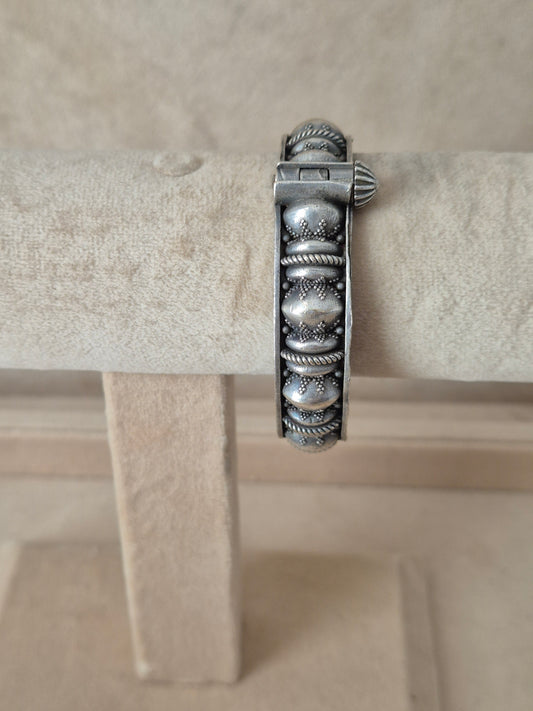 Antique silver oxidized Warisha bangle with textured dome motifs and fine rope-twist borders, displayed on a beige fabric jewelry stand.  by naitri.in