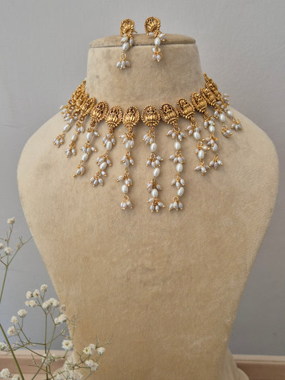 Gold-plated Wayamika choker necklace with intricate traditional leaf patterns and long, hanging white pearl strands ,with a matching pair of drop earrings by naitri.in