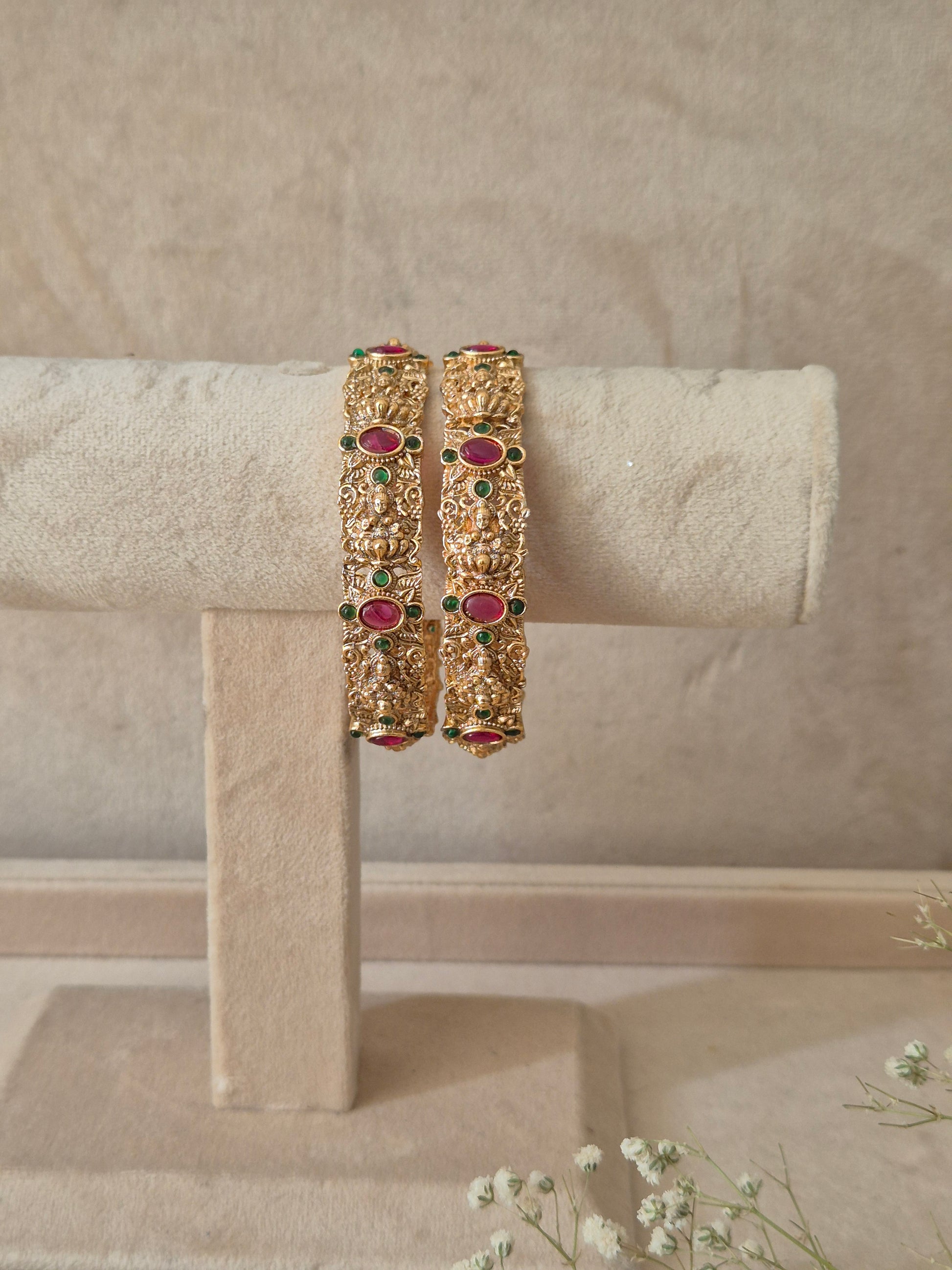 A set of two gold-plated Wibha bangles featuring intricate traditional filigree metalwork inlaid with red and green gemstones by naitri.in