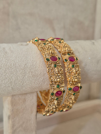 Close-up of Naitri Wibha premium gold ethnic bangle set with traditional Indian floral motifs and vibrant red and green stone accents. by naitri.in