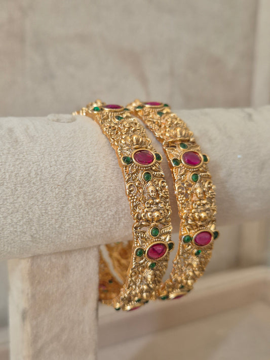 Close-up of Naitri Wibha premium gold ethnic bangle set with traditional Indian floral motifs and vibrant red and green stone accents. by naitri.in