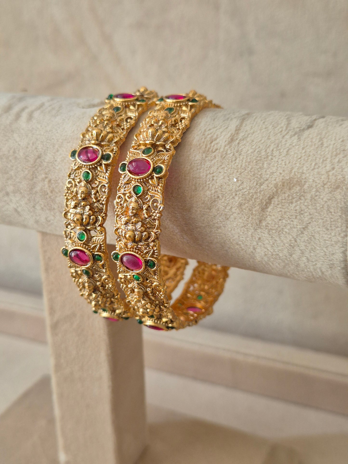 Set of two traditional gold-toned festive bangles with red and green gemstones Elegant golden statement bangles with ethnic gemstone details by naitri.in