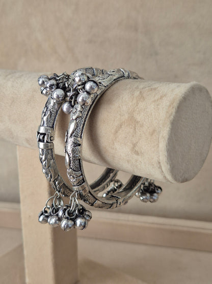 Statement mixed-metal bohemian Kada bangle set featuring intricate floral cutout textures and hanging ghungroo accents, exhibited on a luxury jewelry display holder by naitri.in
