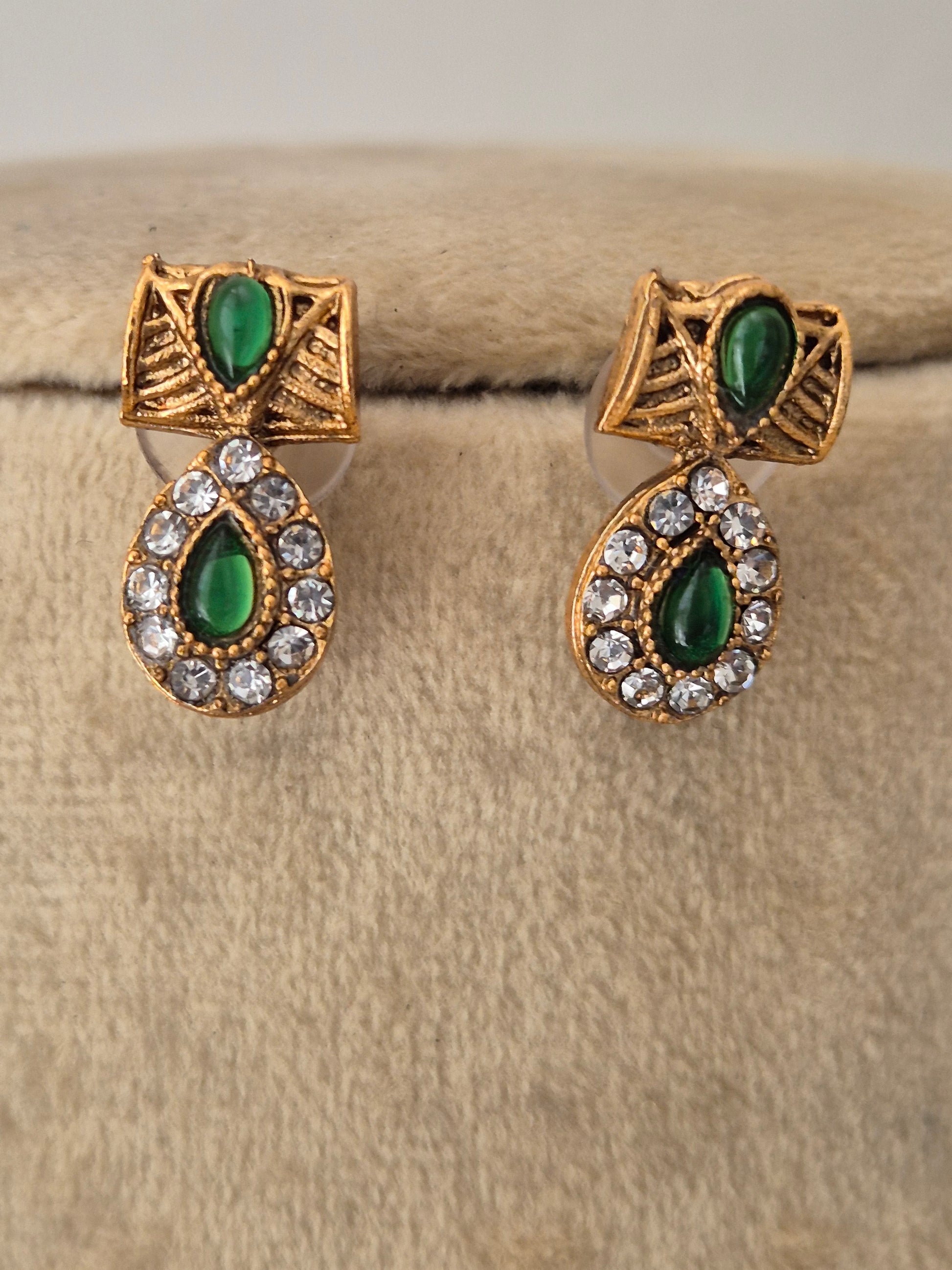 A pair of gold-toned drop earrings with green teardrop-shaped stones and clear rhinestone accents, by naitri.in