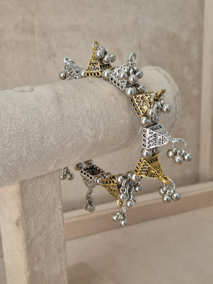 Dual-toned gold and silver Yachana bangle with textured geometric blocks and hanging silver ghungroo charms. Elegant dual-tone ethnic cuff bracelet with traditional festive details, by naitri.in