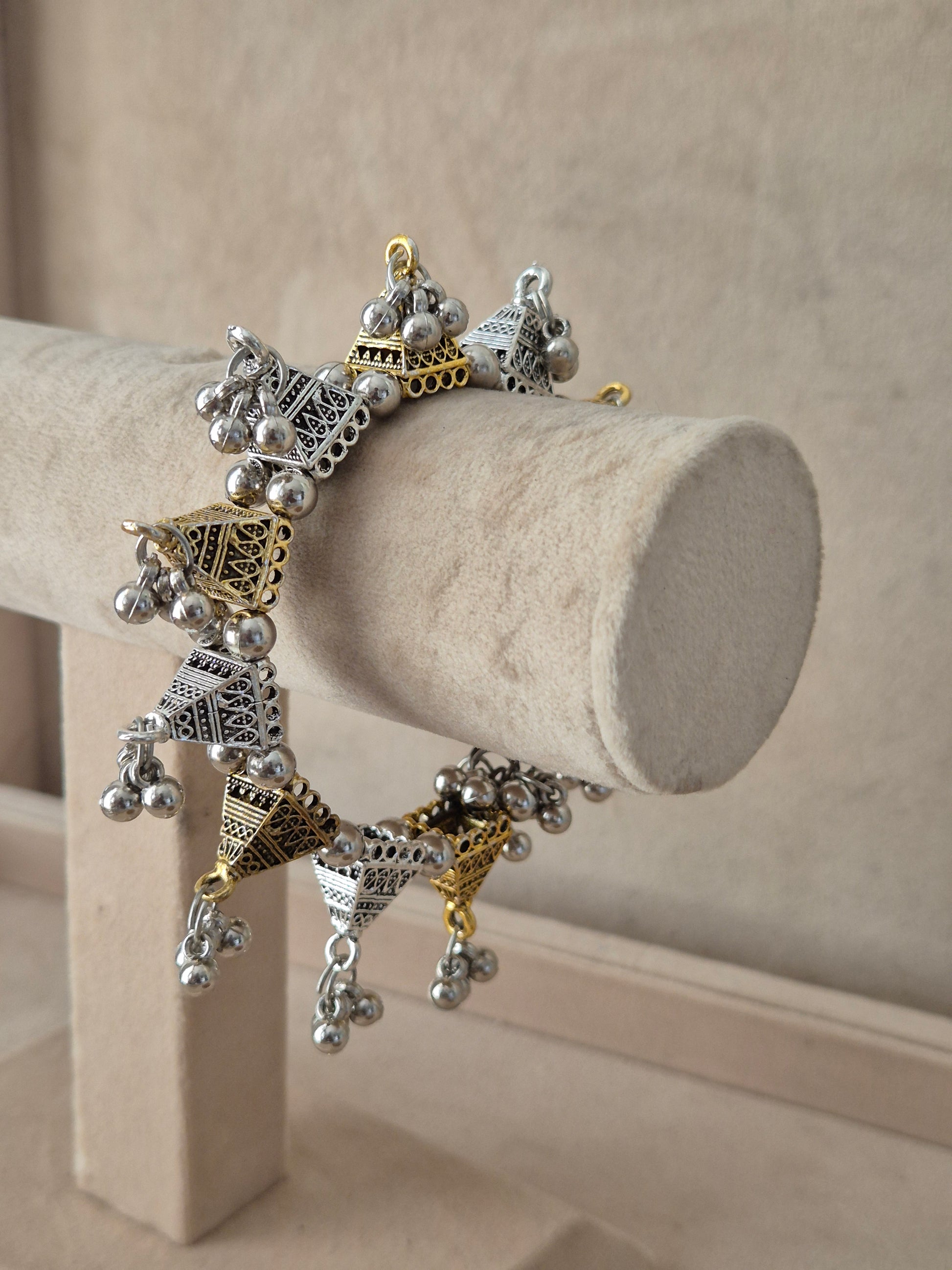 Wide statement bohemian Kada bangle featuring intricate horizontal bands of gold-toned patterns, silver-plated filigree accents, and loud dangling metallic bells by naitri.in
