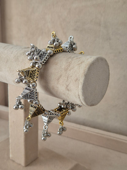 Wide statement bohemian Kada bangle featuring intricate horizontal bands of gold-toned patterns, silver-plated filigree accents, and loud dangling metallic bells by naitri.in