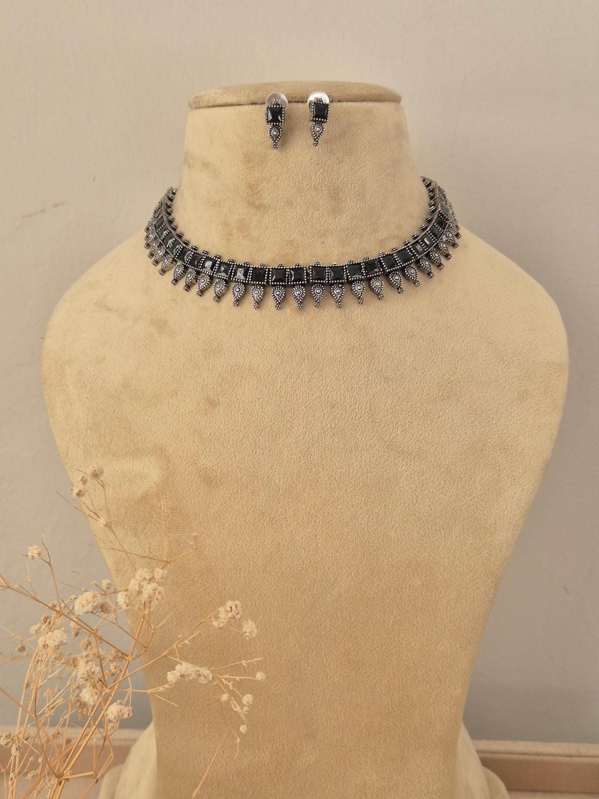 A silver-toned choker necklace and matching drop earrings  The necklace features a row of colorful rectangular gemstones in black with dangling silver teardrop-shaped charms by naitri.in