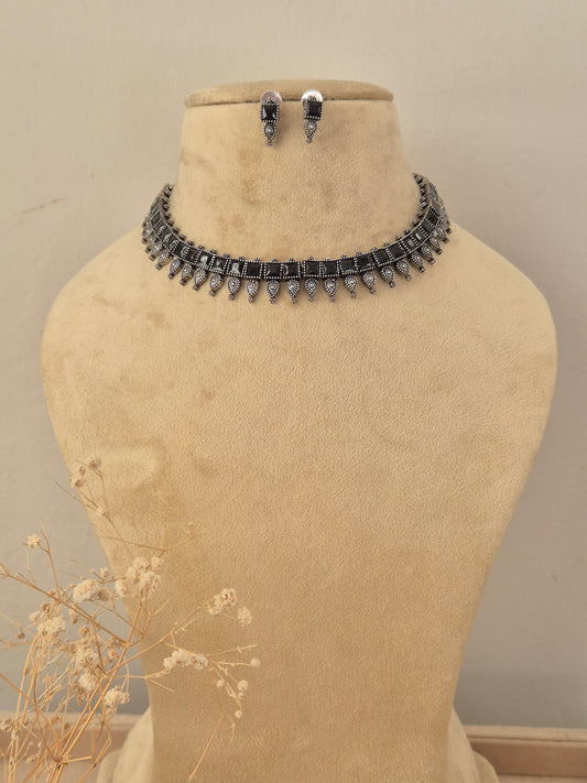 A silver-toned choker necklace and matching drop earrings  The necklace features a row of colorful rectangular gemstones in black with dangling silver teardrop-shaped charms by naitri.in