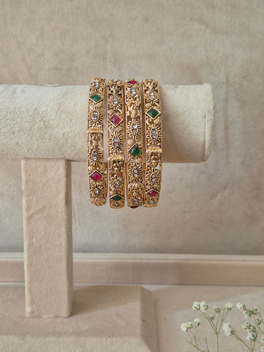 A set of four gold-plated Yamini bangles featuring intricate floral and textured metalwork inlaid with alternating red and green gemstones by naitri.in