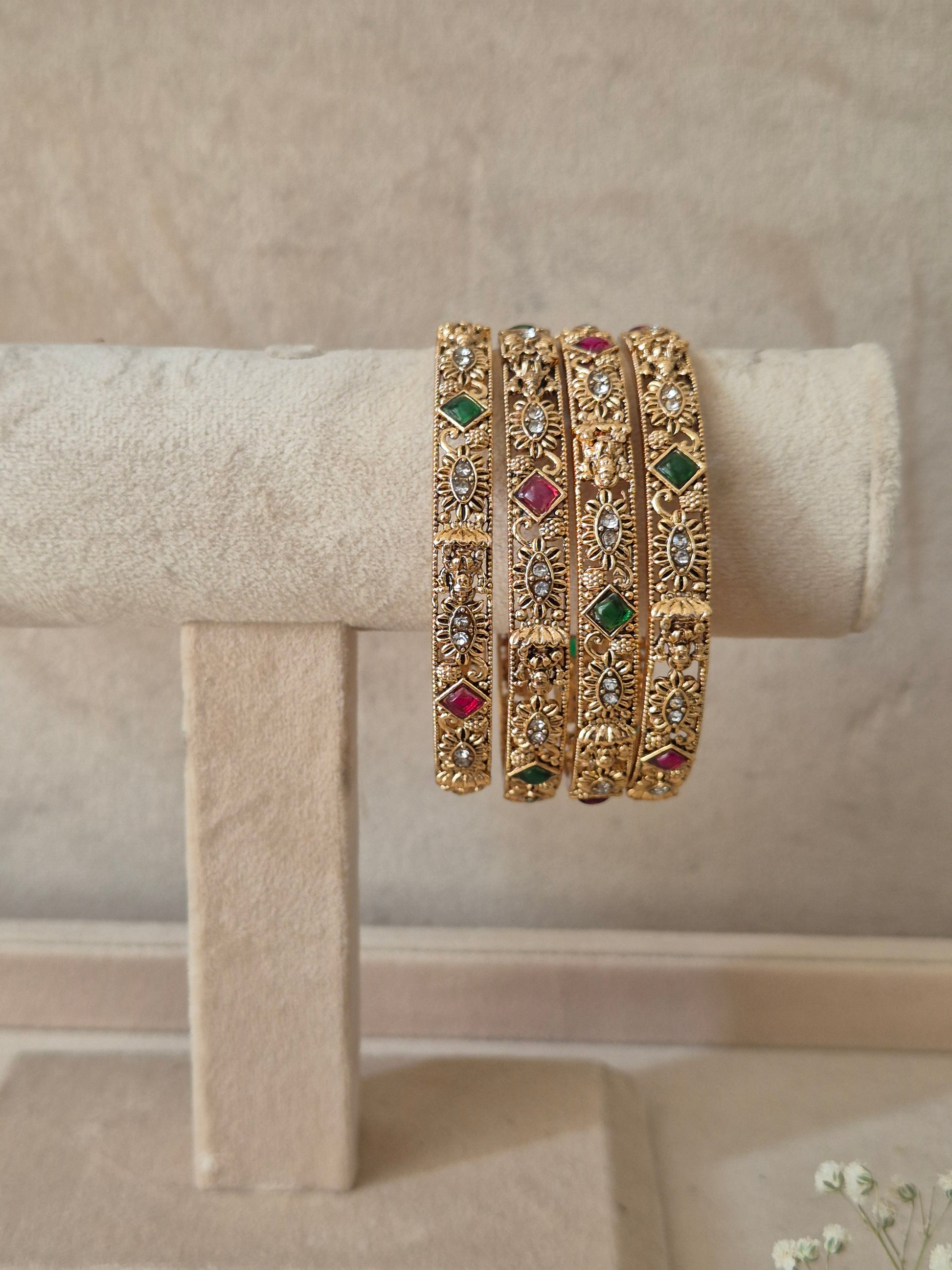 Set of four traditional gold-toned festive bangles with red and green gemstones by naitri.in