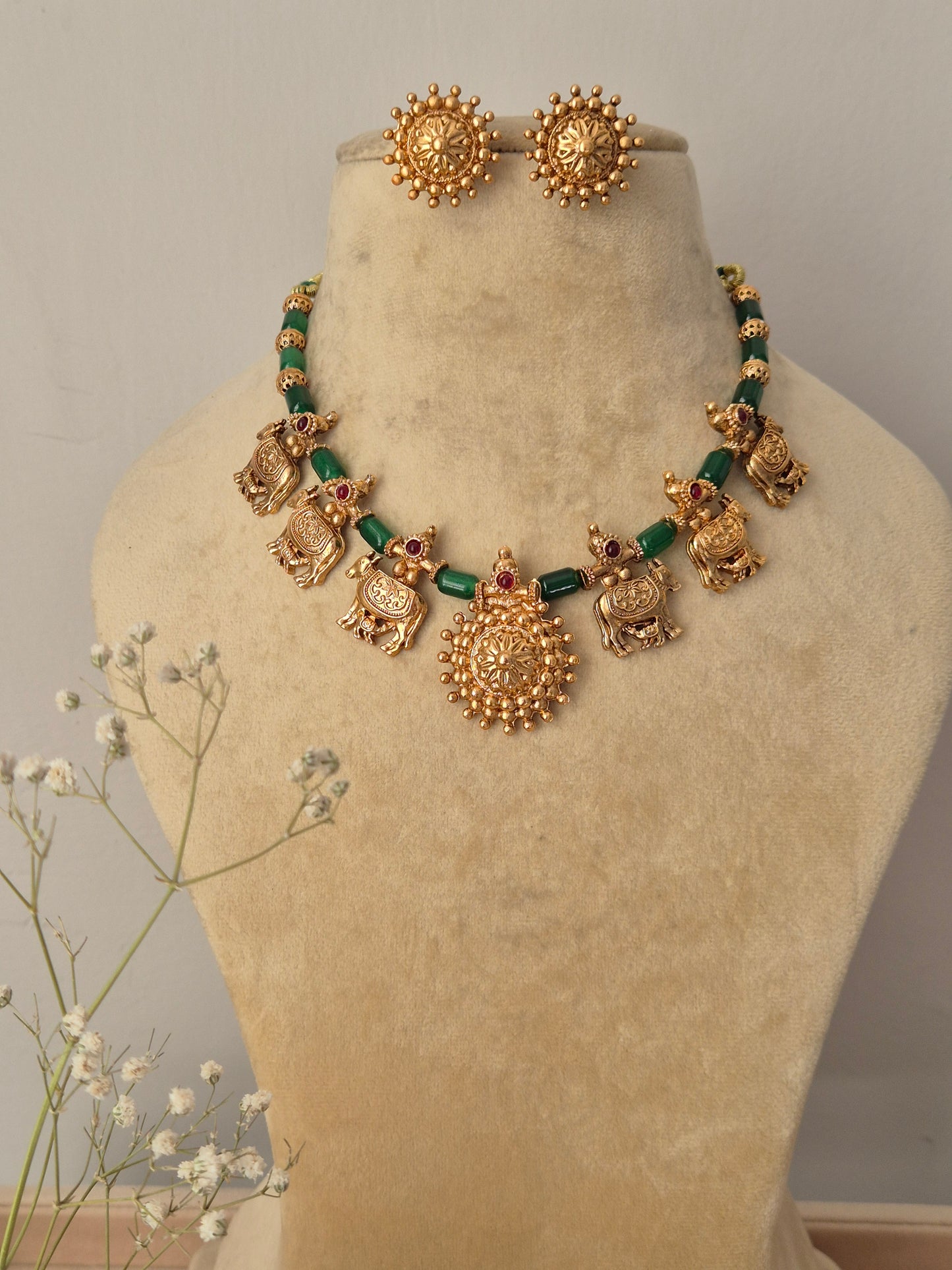 Set featuring gold-toned temple jewelry with mother-baby cow motifs, green beads, and matching circular stud earrings by naitri.in