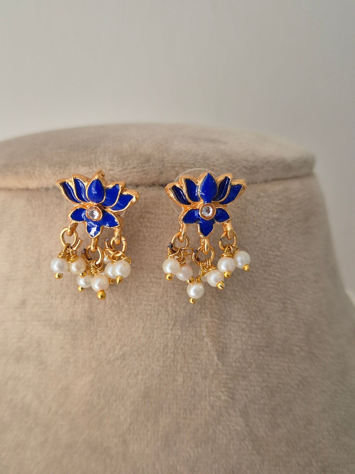 Pair of gold earrings with blue petals and leaves and white pearls a small stone in the middle minimal and aesthetic design by naitri.in 