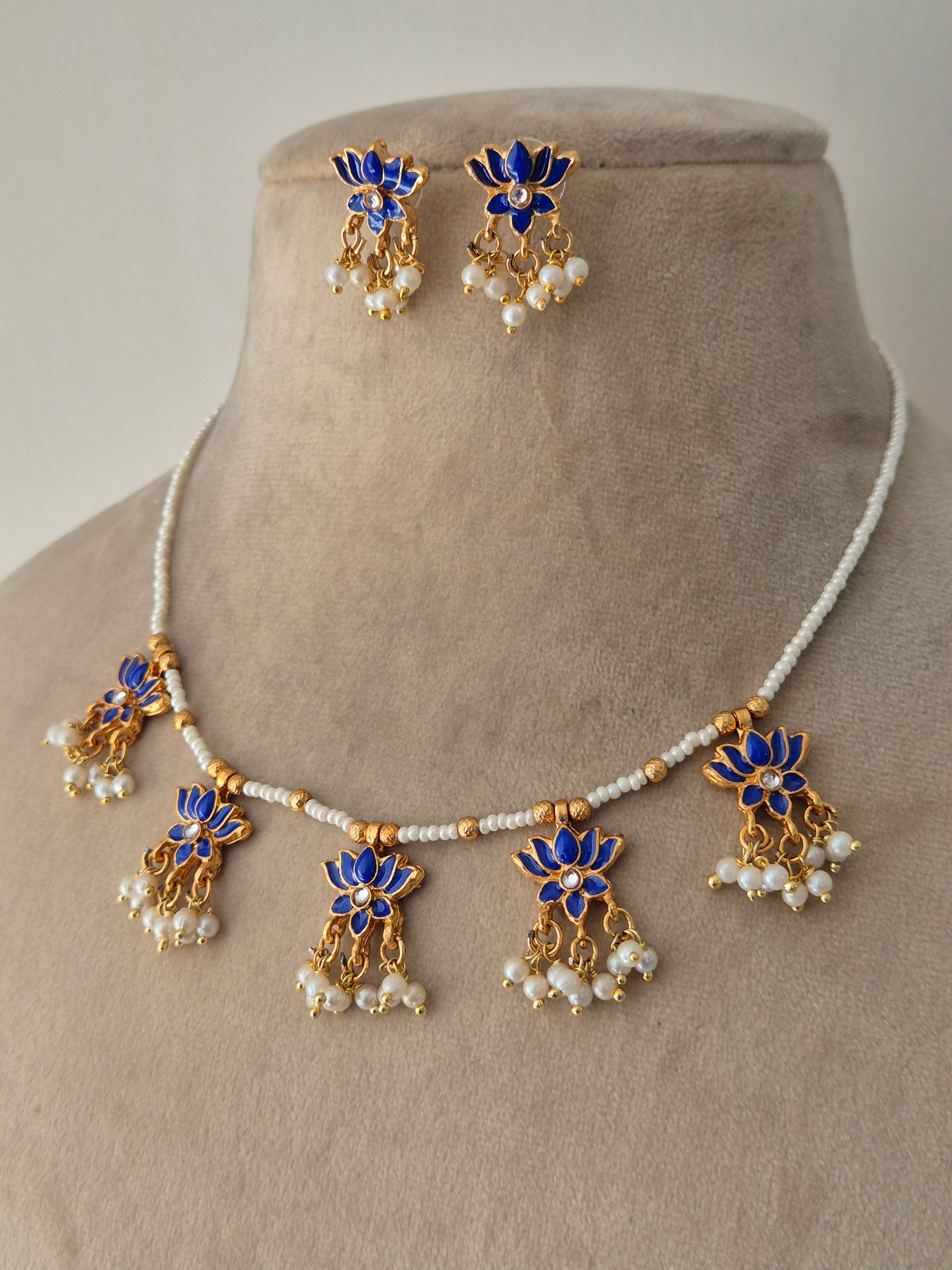 Jewelry set with blue and gold elements with Pair of gold earrings with blue petals and leaves, a small stone in the middle and white pearls by naitri.in