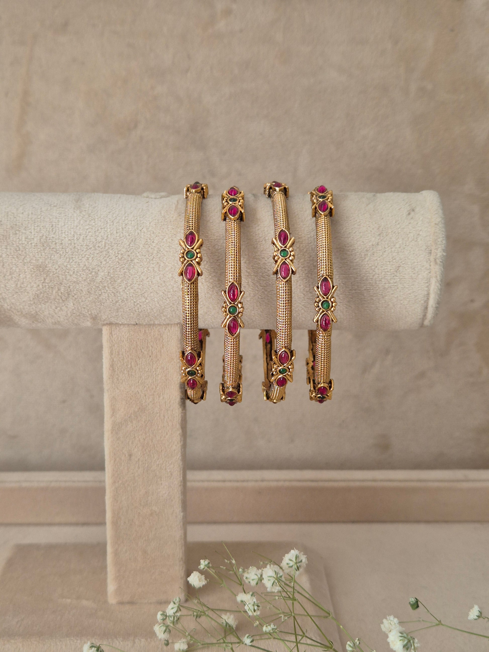 set of 4 antique gold-plated bangles featuring intricate metalwork and ruby-red and green stone embellishments by naitri.in