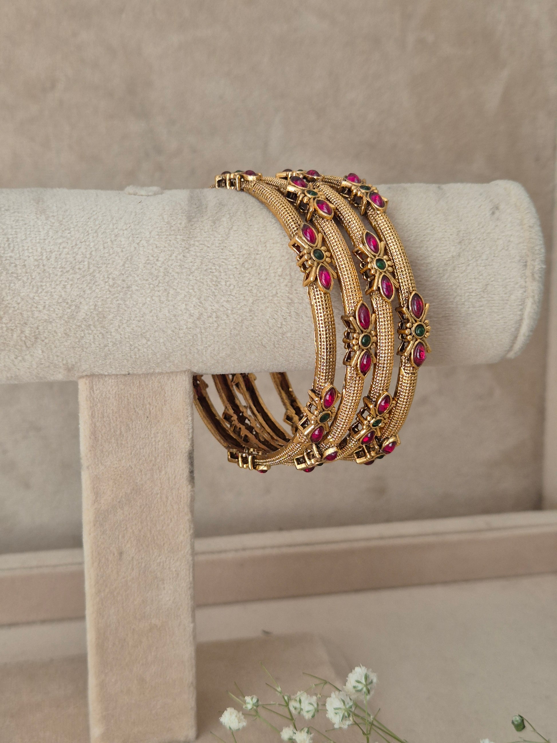  set of 4 antique gold-plated bangles featuring intricate metalwork and ruby-red and green stone embellishments by naitri.in