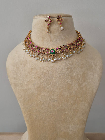 Gold-plated featuring pink stone floral motifs, a central green stone, and white pearl bead droplets, with matching floral stud earrings by naitri.in