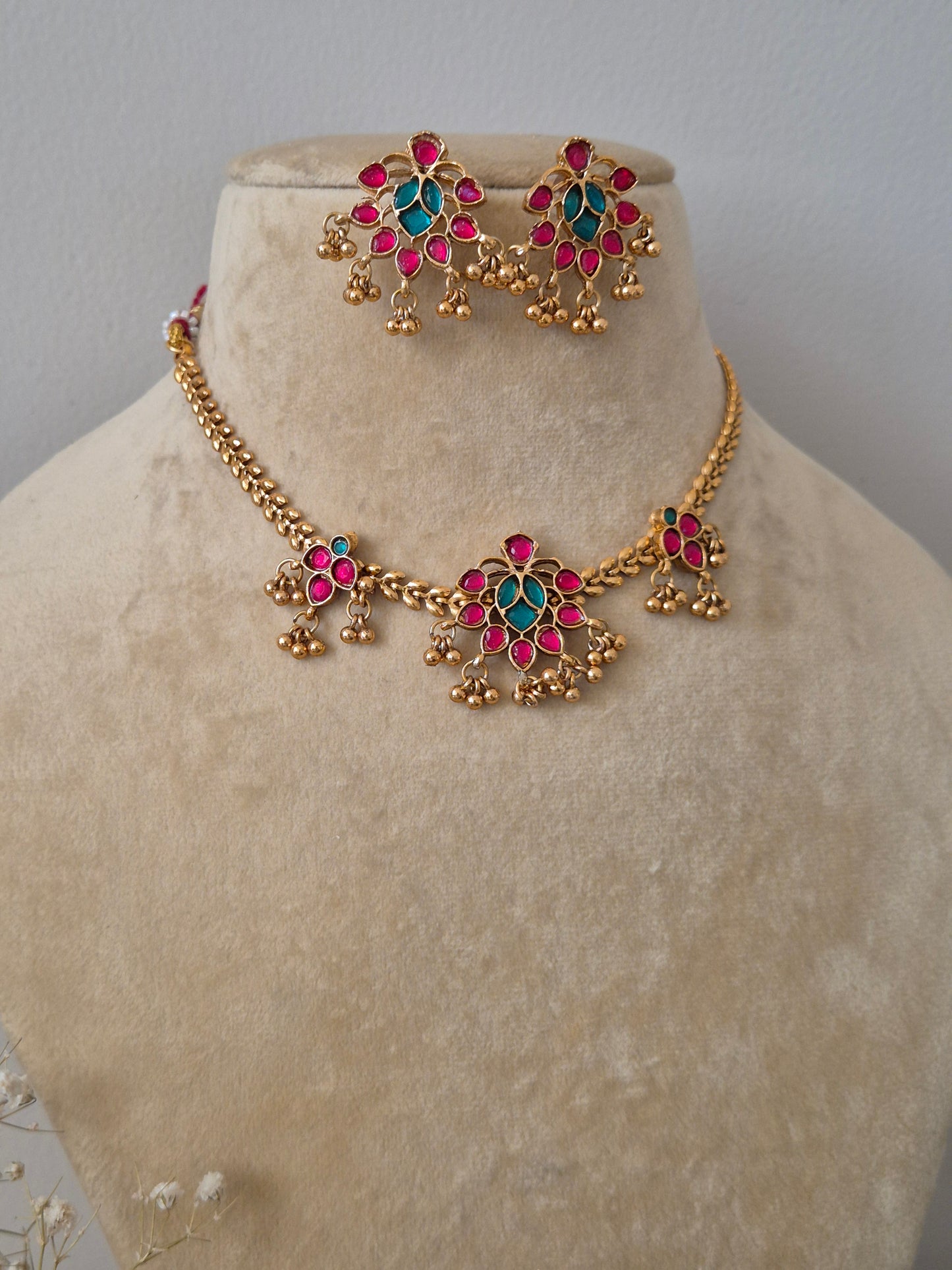 Handcrafted jewelry set in brass alloy with a polished golden finish, featuring traditional floral motifs and vibrant pink and green stones by naitri.in
