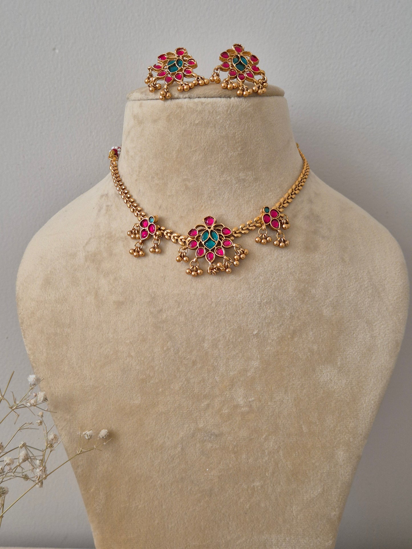 Necklace Set featuring a gold-toned choker with floral pendant and red and green gemstone accents, paired with matching floral stud earrings by naitri.in