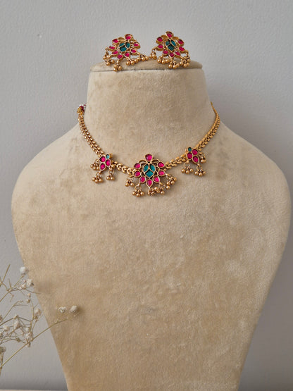 Necklace Set featuring a gold-toned choker with floral pendant and red and green gemstone accents, paired with matching floral stud earrings by naitri.in