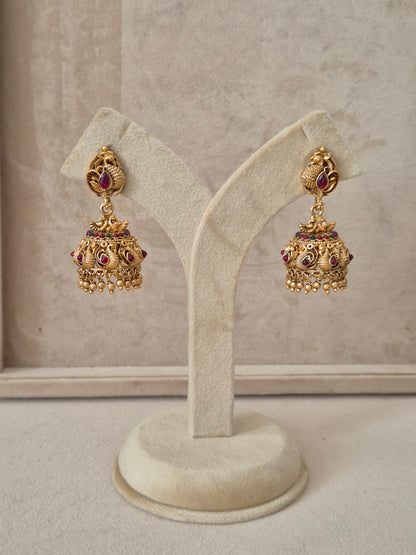 Intricately designed gold-plated jhumka earrings featuring peacock motifs, ruby red stones, and a band of tiny green beads by naitri.in