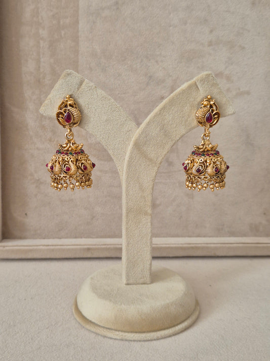 Intricately designed gold-plated jhumka earrings featuring peacock motifs, ruby red stones, and a band of tiny green beads by naitri.in