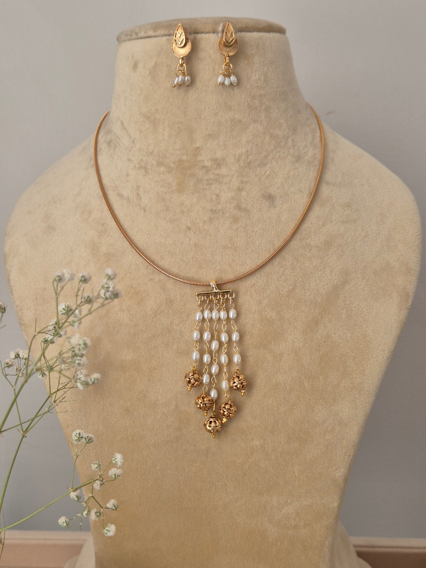 Set featuring a gold-tone minimalist chain with a cascading white pearl and gold bead tassel pendant and matching leaf-style earrings by naitri.in