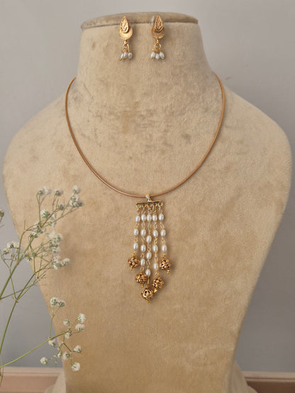 Set featuring a gold-tone minimalist chain with a cascading white pearl and gold bead tassel pendant and matching leaf-style earrings by naitri.in