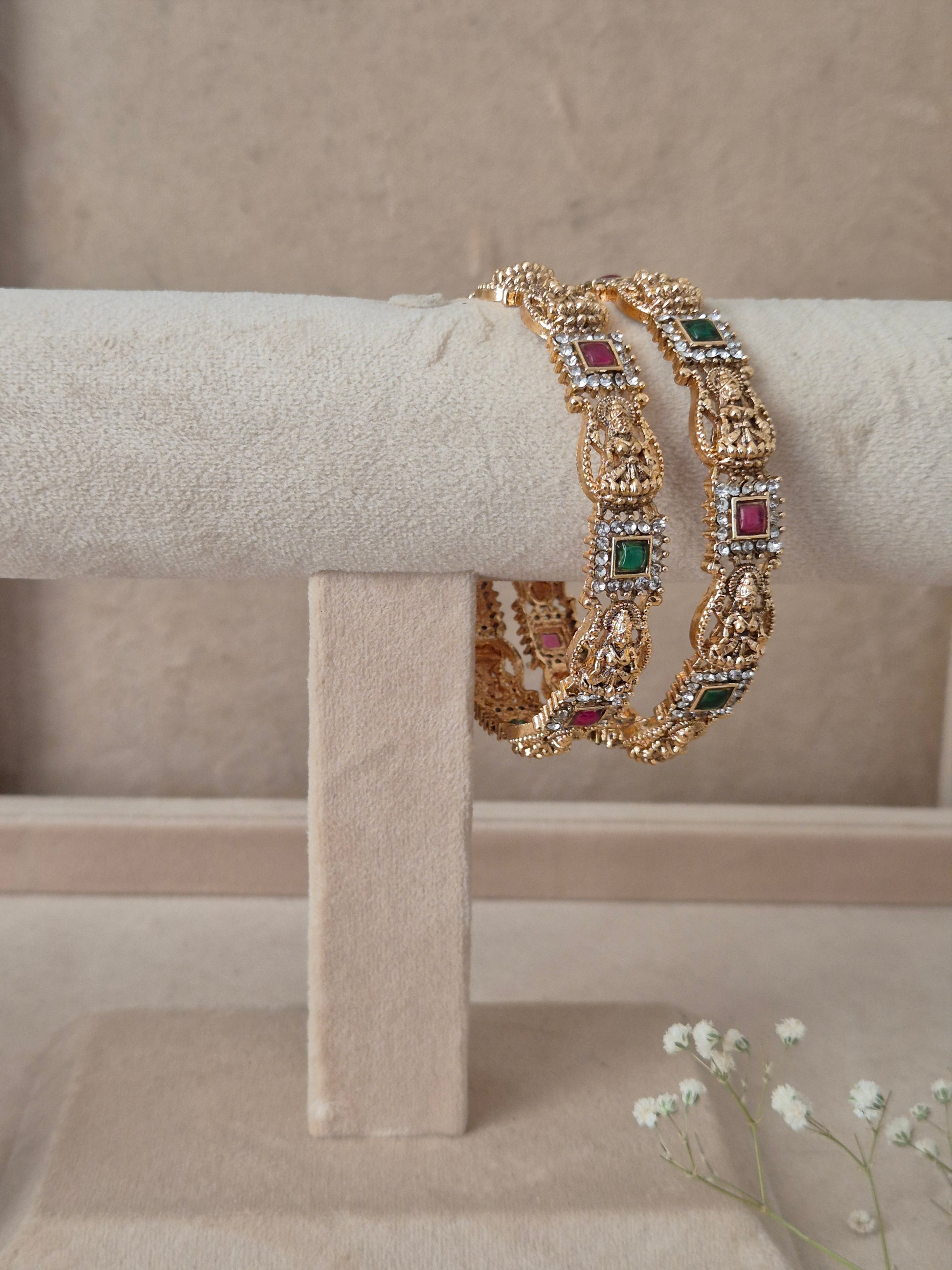 Pair of Naitri's Yogshi gold bangles showcasing detailed antique craftsmanship, embedded with vibrant pinkish-red and green accent stones, by naitri.in