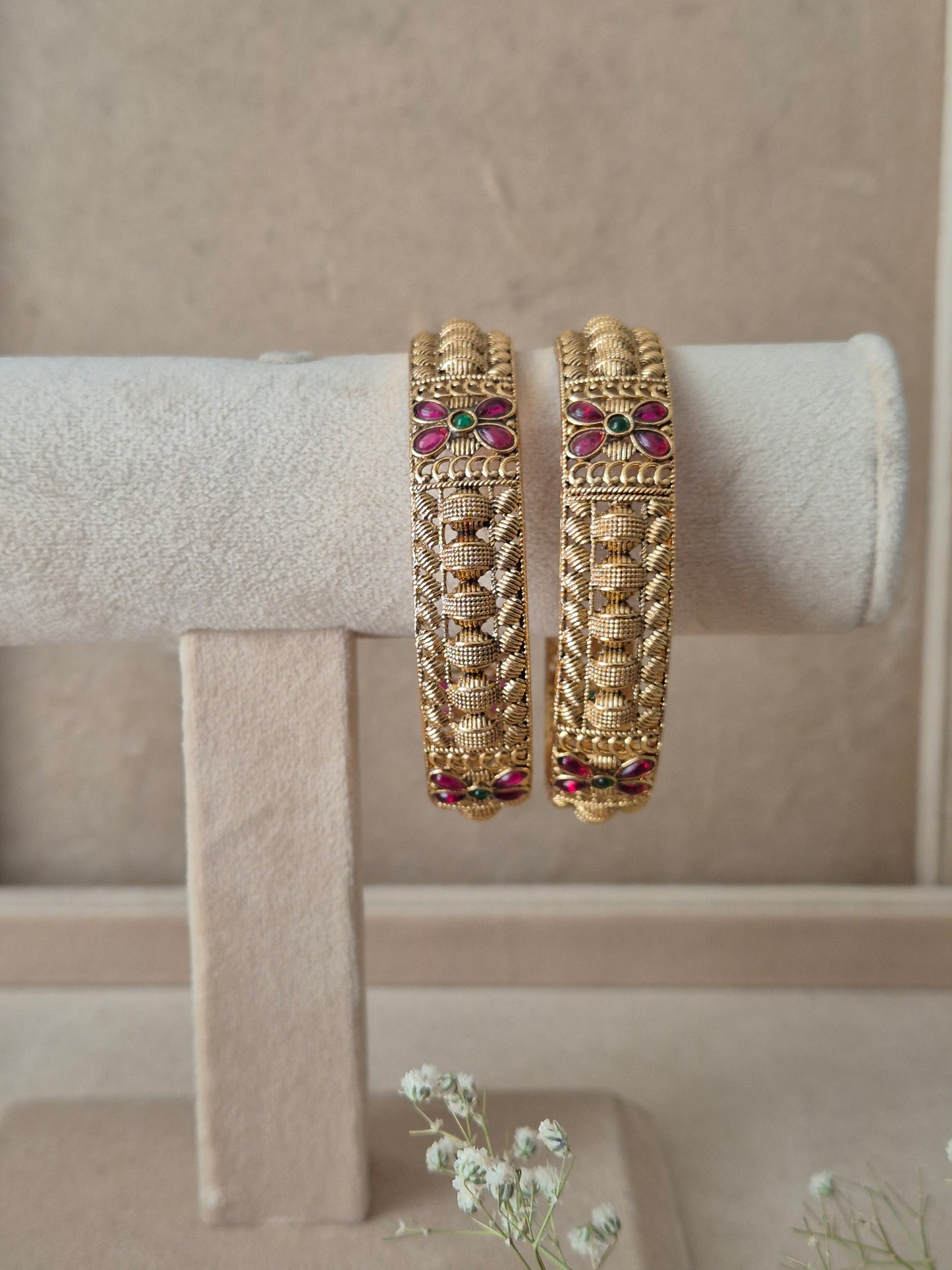 Set of 2 Zahira gold bangles by Naitri featuring intricate traditional filigree and leaf patterns, accented with ruby-red and emerald-green floral gemstones by naitri.in