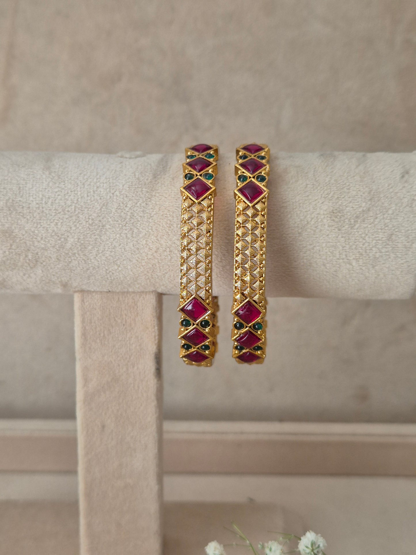 A pair of gold-plated bangle bracelets with red and green stone accents, by naitri.in