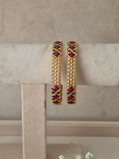A pair of gold-plated bangle bracelets with red and green stone accents, by naitri.in