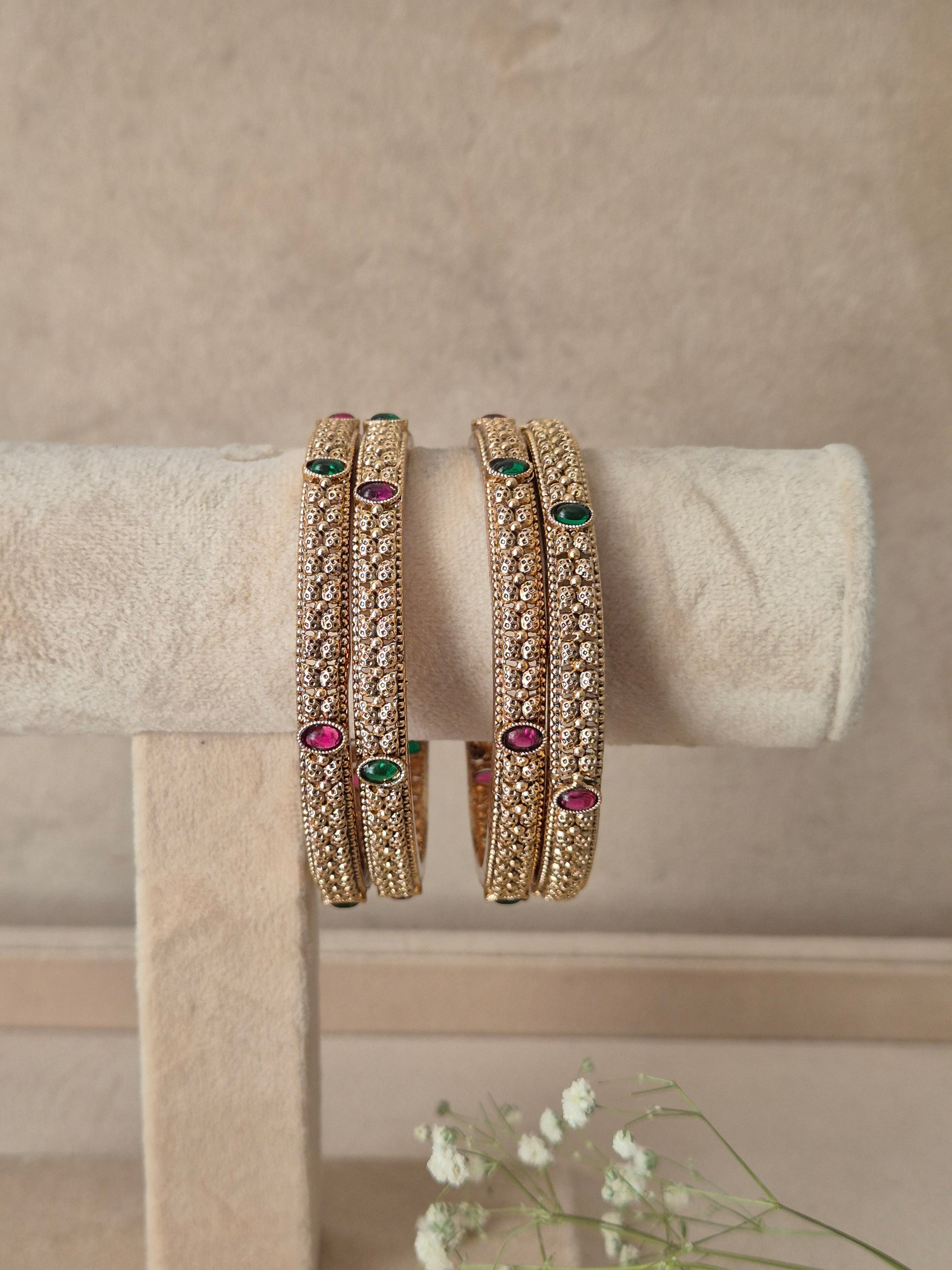 Three gold-plated bangles with intricate gold-toned filigree and small green and pink gemstone accents, for festive and wedding wear by naitri.in