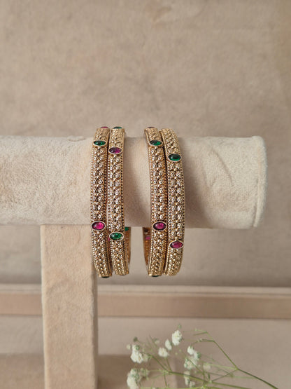 Three gold-plated bangles with intricate gold-toned filigree and small green and pink gemstone accents, for festive and wedding wear by naitri.in