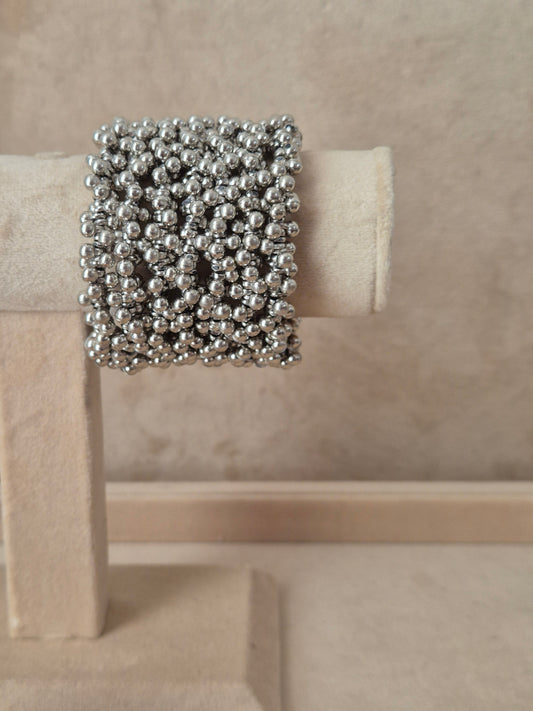 Silver-toned Zani Spiral bangle featuring rows of tightly clustered metallic beads, displayed on a beige fabric jewelry stand by naitri.in