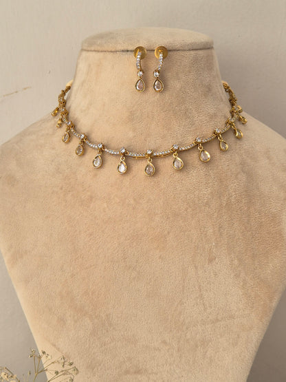 Gold-toned jewelry set featuring a delicate chain necklace with dangling teardrop-shaped clear stones and matching drop earrings by naitri.in