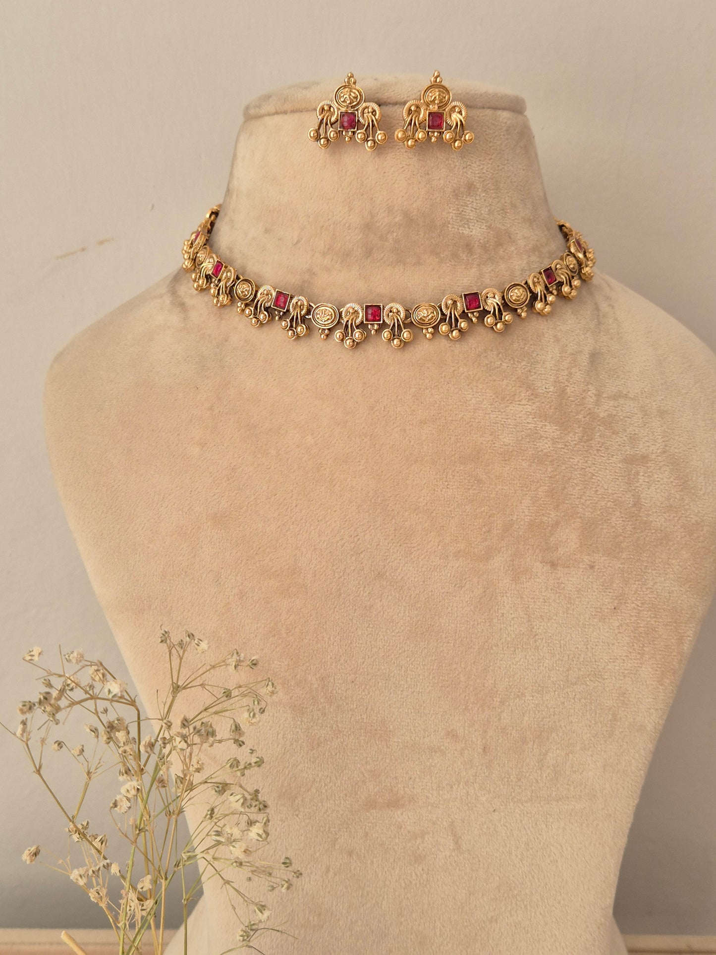 Gold-toned traditional Indian jewelry set featuring a necklace with red stones and matching earrings, by naitri.in