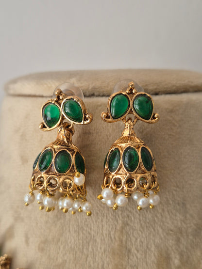 A pair of gold-plated Indian jhumka earrings with green stone inlays and dangling white pearl beads, by naitri.in