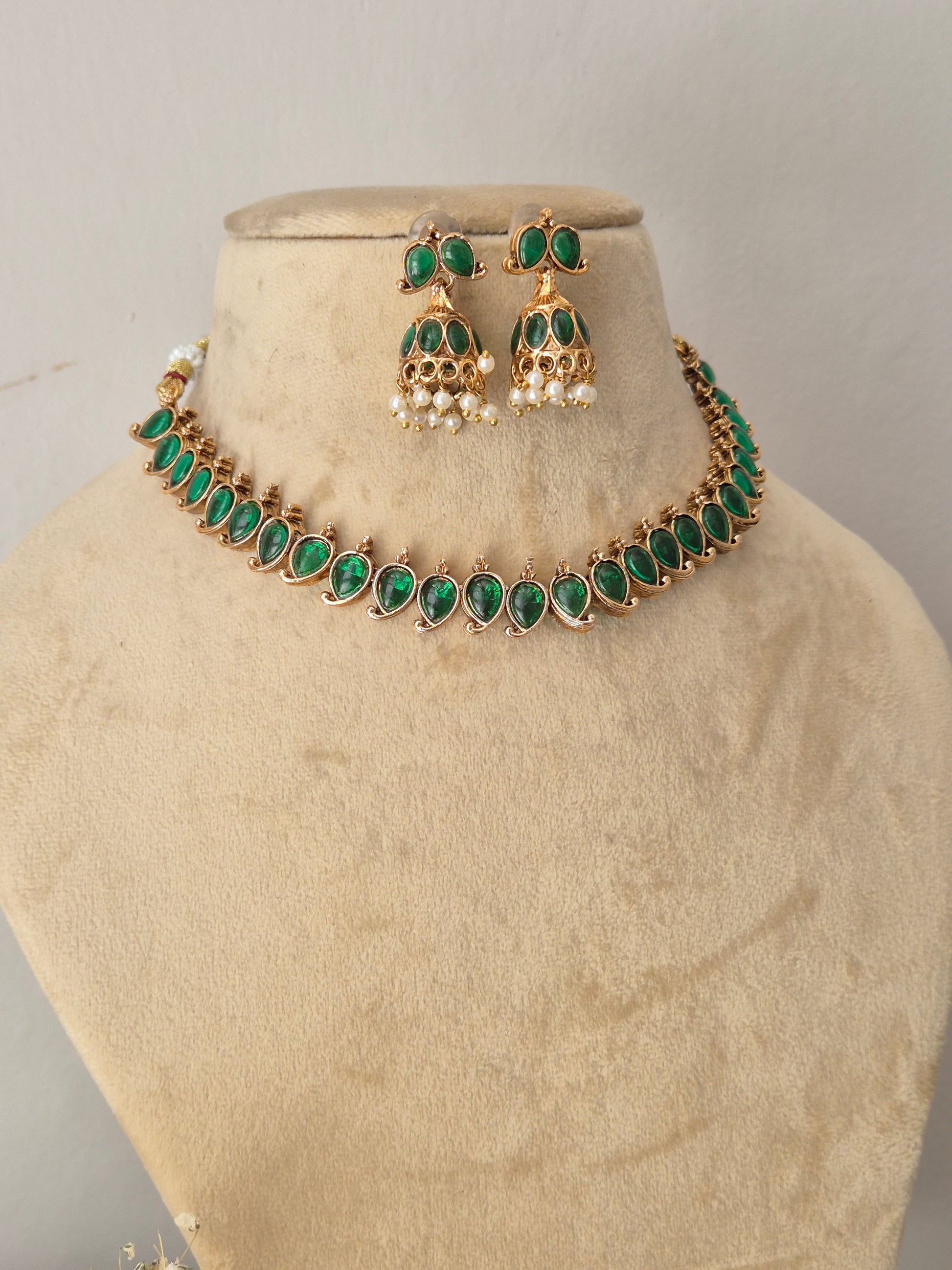 Gold-tone jewelry set with green stones and white pearl-like accents, green stone choker and matching traditional pearl-drop jhumka earrings by naitri.in