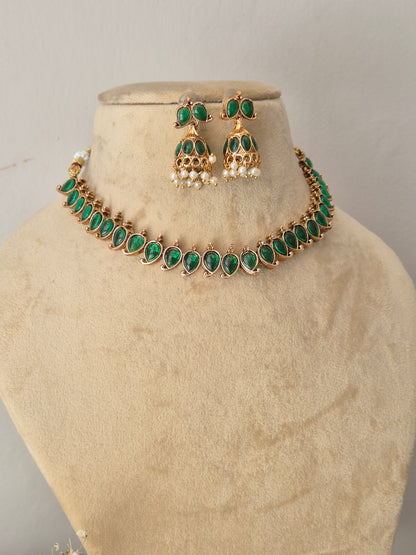 Gold-tone jewelry set with green stones and white pearl-like accents, green stone choker and matching traditional pearl-drop jhumka earrings by naitri.in