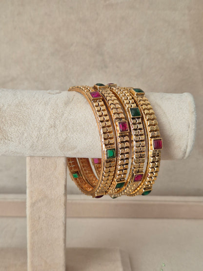 A set of four gold-plated bangles with textured patterns and small square green and pink stone accents, by naitri.in